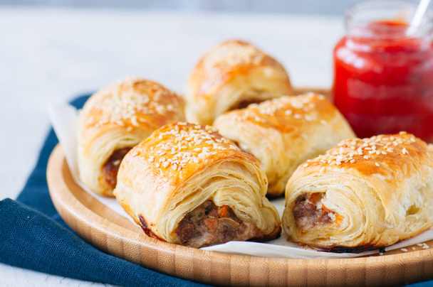 Beef and caramelised onion sausage rolls on a wooden plate with  - Фото, изображение