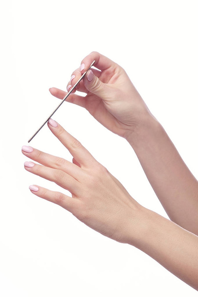 Un primer plano de la mano de una joven mujer limando uñas, sobre un fondo blanco
. - Foto, imagen