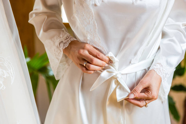 Ніжна молода сексуальна дівчина зв'язала халат. Ніжні руки торкаються білого халата вранці
 - Фото, зображення