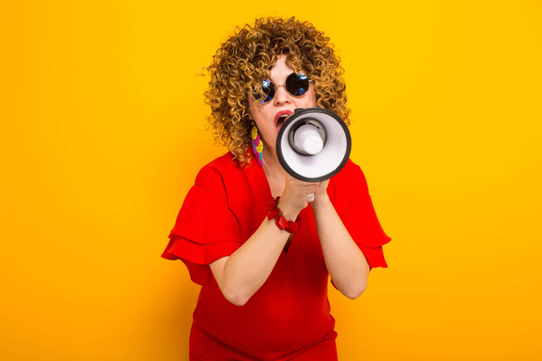Attractive young curly haired woman in red dress and sunglasses with loudspeaker - Fotografie, Obrázek