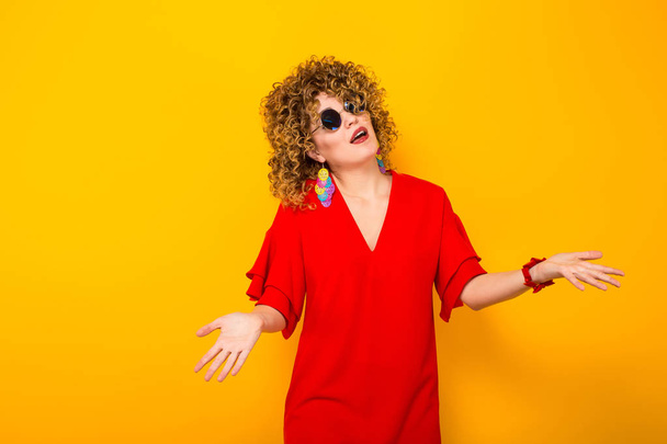 Attractive young curly haired woman in red dress and sunglasses  gesticulating  - Photo, Image