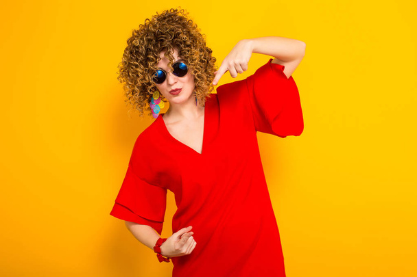 Attractive young curly haired woman in red dress and sunglasses  pointing - Zdjęcie, obraz