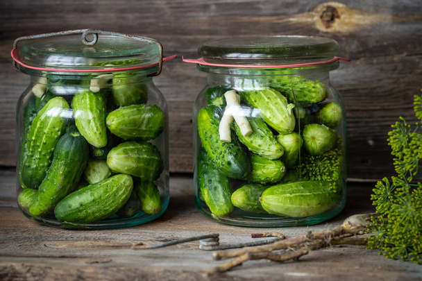 Potten van ingemaakte gemarineerde komkommers op rustieke tafel  - Foto, afbeelding