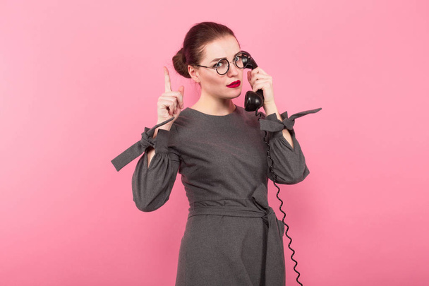 Jovem morena atraente em óculos falando no telefone antigo contra fundo rosa
  - Foto, Imagem