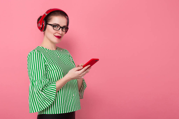 Привлекательная молодая брюнетка в красных наушниках с использованием смартфона на розовом фоне студии
  - Фото, изображение