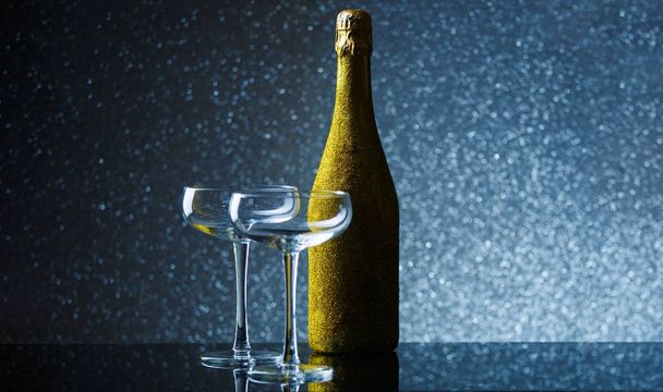 Picture of bottle of champagne in gold wrapper with empty wine glass on gray background - Foto, Imagem