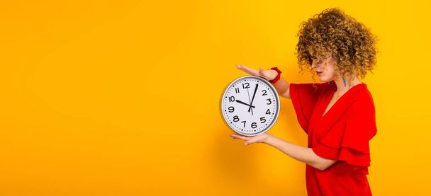 Attractive young curly haired woman in red dress holding wall clock - Photo, Image