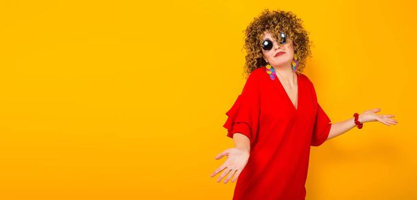 Attractive young curly haired woman in red dress and sunglasses showing she doesn't know - Fotó, kép