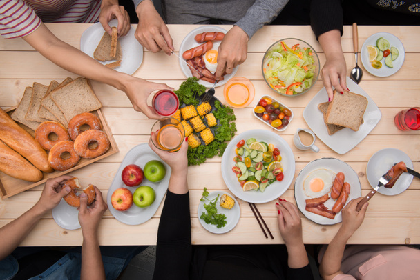 U geniet van een diner met vrienden. Bovenaanzicht van groep mensen eten samen zitten op houten tafel - Foto, afbeelding