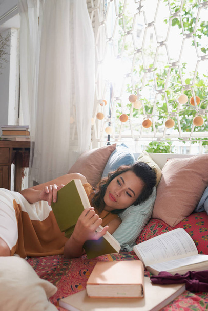 Mujer joven y bonita acostada en la cama con muchos libros alrededor
 - Foto, imagen