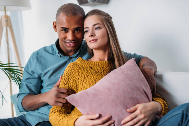 affectionate multicultural couple hugging on sofa  - Foto, afbeelding