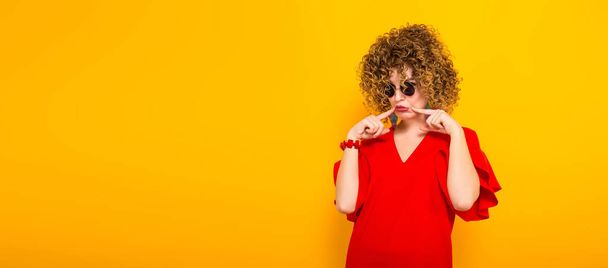 Attractive young curly haired woman in red dress and sunglasses making sad face - Fotoğraf, Görsel