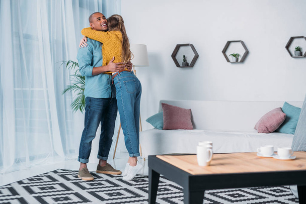 smiling multicultural couple hugging in room - Photo, image