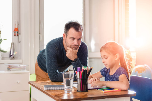 Father lean on the desk next to daughter helping her to finish homework - Photo, Image