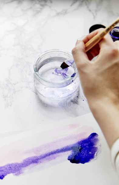 female artist dipping brush with ultra violet paint into water, artist workplace concept  - Foto, imagen