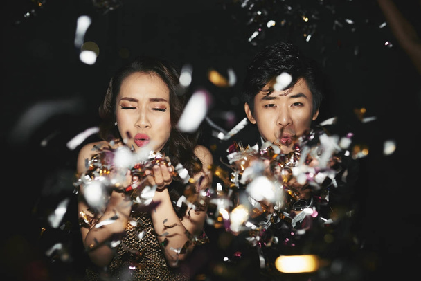 Joven pareja vietnamita soplando confeti en la cámara
 - Foto, Imagen