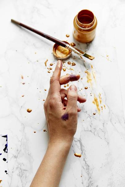view of female artist hand soiled with golden and violet paints on white background, artist workspace concept  - Foto, afbeelding