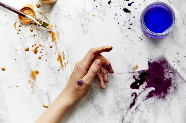 view of female artist hand soiled with golden and violet paints on white background, artist workspace concept  - 写真・画像
