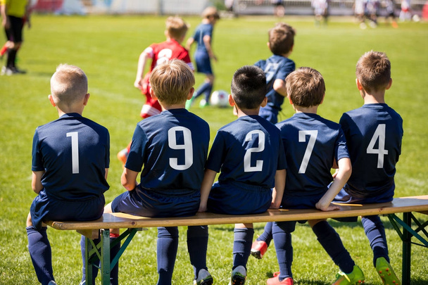 Kids sport team sitting on a bench. Group of kids soccer players. Children football club. Football soccer tournament game for children. Boys kicking soccer ball on grassy pitch. Children play sports outdoors. - Photo, Image