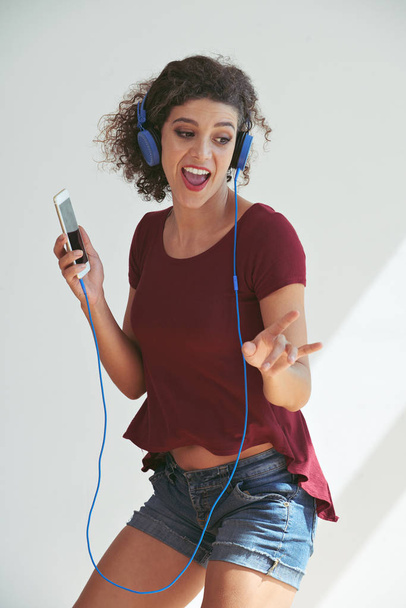 Cheerful young woman in casual clothes dancing to the music she is listening to - Фото, изображение