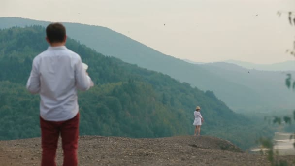 The back view of the lost traveller holding the map and looking at the blonde woman standing on the edge of the mountains. Copter view. - Video, Çekim
