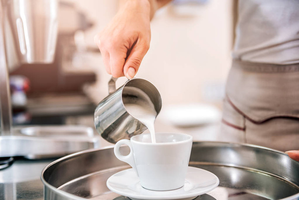 Woman pouring cream or milk into cup of coffee - Foto, Imagen