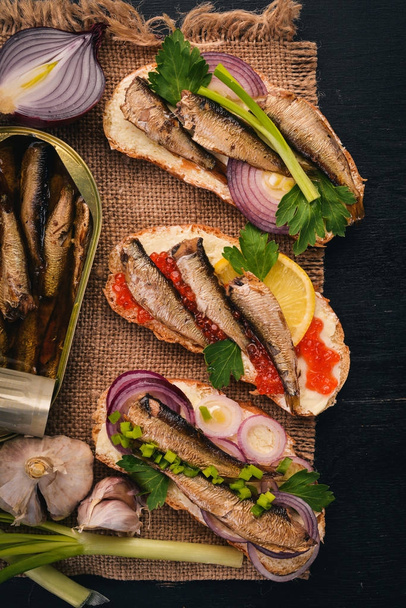 A set of sandwiches with sprats, and caviar, onion and parsley, on a wooden background. Top view. Copy space. - 写真・画像