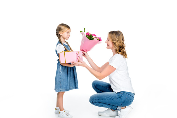 mother and daughter with present and bouquet of flowers, isolated on white - Фото, изображение