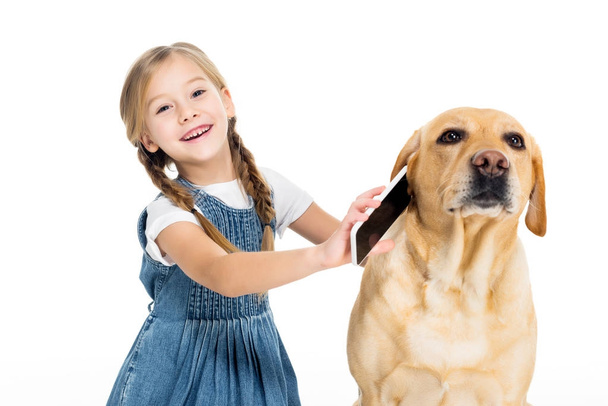 imádnivaló vidám gyermek giving smartphone-hoz kutya, elszigetelt fehér - Fotó, kép