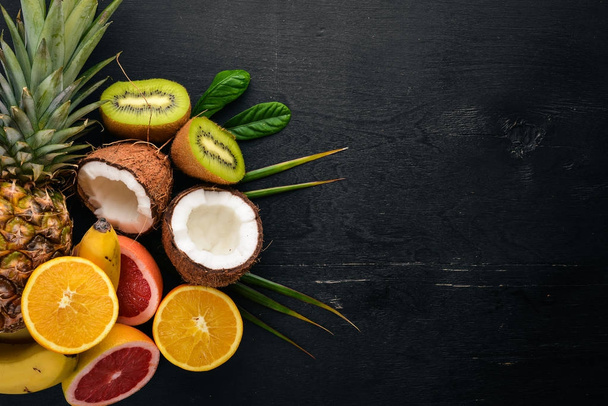 Fresh Tropical Fruits. Pineapple, coconut, kiwi, orange, pomegranate, grapefruit. On a wooden background. Top view. Free space for text. - Foto, Imagem