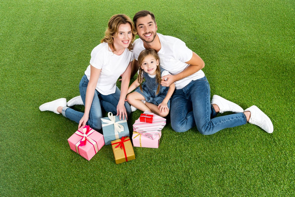 high angle view of family with wrapped gifts sitting on green grass - Фото, изображение