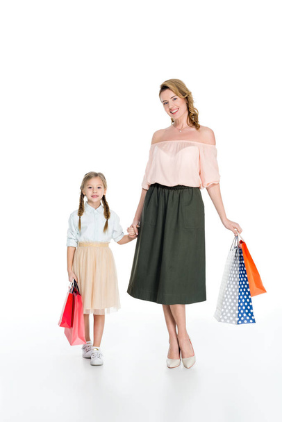 stylish mother and daughter with shopping bags holding hands isolated on white - Фото, изображение