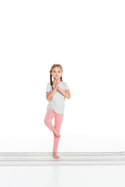 kind het beoefenen van yoga op de yoga mat geïsoleerd op wit - Foto, afbeelding