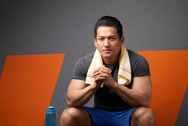 Portrait of smiling Vietnamese fit man sitting in gym checkroom - Photo, Image