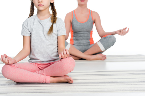 Teilansicht athletischer Mutter und Tochter beim Yoga auf Matten isoliert auf weißem Grund - Foto, Bild