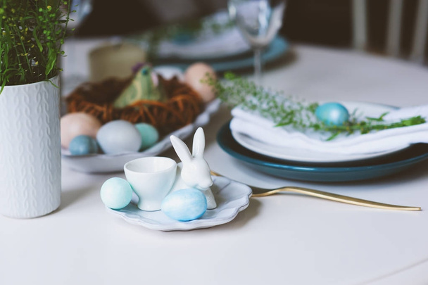 easter and spring festive table in nordic scandinavian style, decorated in blue and white natural tones with eggs, bunny, fresh flowers and candles. - Фото, зображення