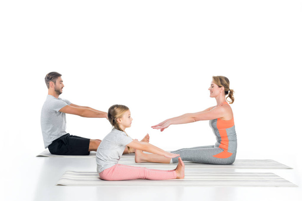 side view of parents and daughter in sportswear stretching on mats isolated on white - Zdjęcie, obraz