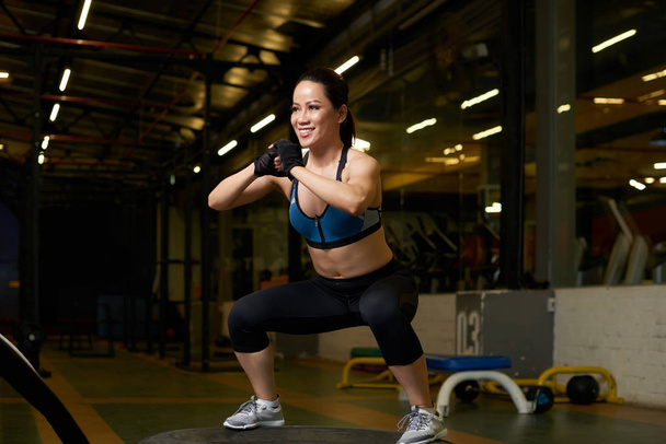 Vidám ázsiai fiatal nő csinál zömök az edzőteremben - Fotó, kép