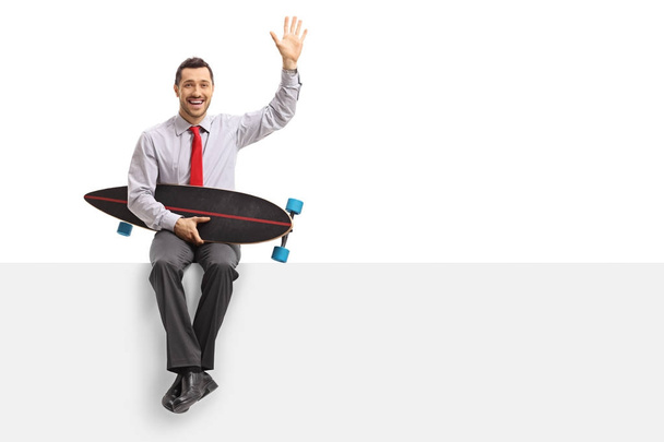 Businessman with a longboard sitting on a panel and waving - Fotografie, Obrázek