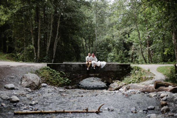 belo casal jovem casamento sentado na ponte acima do rio da montanha em Alpes
 - Foto, Imagem