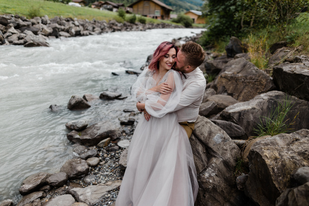 beautiful happy wedding couple hugging and kissing near mountain river in Alps - Photo, Image