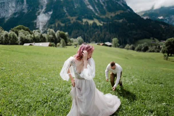 mariée heureuse en robe de mariée et marié marchant sur la prairie de montagne verte dans les Alpes
 - Photo, image