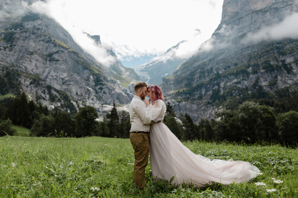 boldog menyasszony és a vőlegény, átölelve a zöld hegyi rétek, felhők, Alpok - Fotó, kép