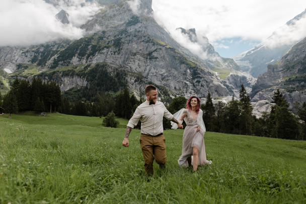 счастливая невеста и жених держатся за руки и ходят по альпийскому лугу с облаками
 - Фото, изображение