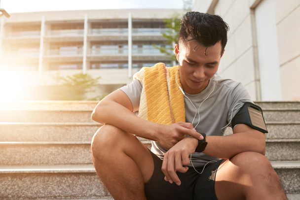 Young Vietnamese man checking smartwatch after jogging in the morning - Photo, Image