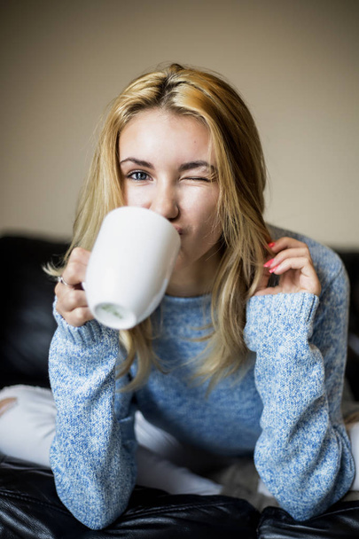 Zachte portret van tienermeisje drinken warme koffie thuis en winking - Foto, afbeelding