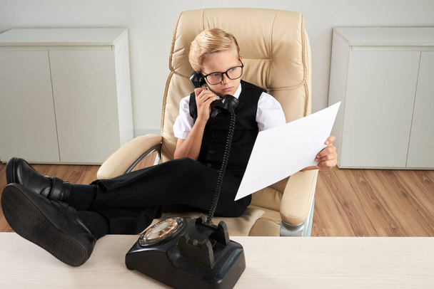 Confident little businessman reading document and calling on telephone - Foto, Bild
