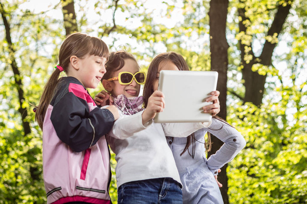 Photo of three little girls with tablet in green park  - Fotoğraf, Görsel