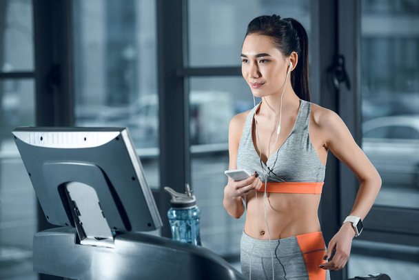 young athletic sportswoman using smartphone on treadmill at gym - Photo, Image