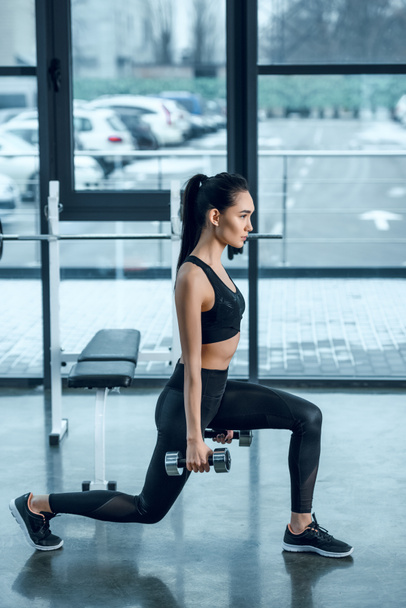 vue latérale de la jeune femme en forme faisant squats jambe unique avec haltères à la salle de gym
 - Photo, image